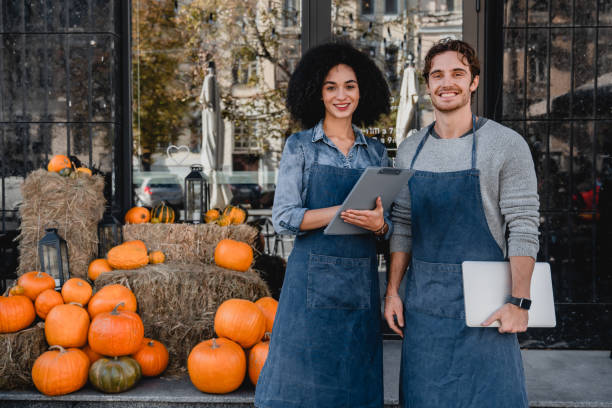 Two smiling seasonal workers in aprons stand with pumpkins and hay, suggesting reasons to retain them.